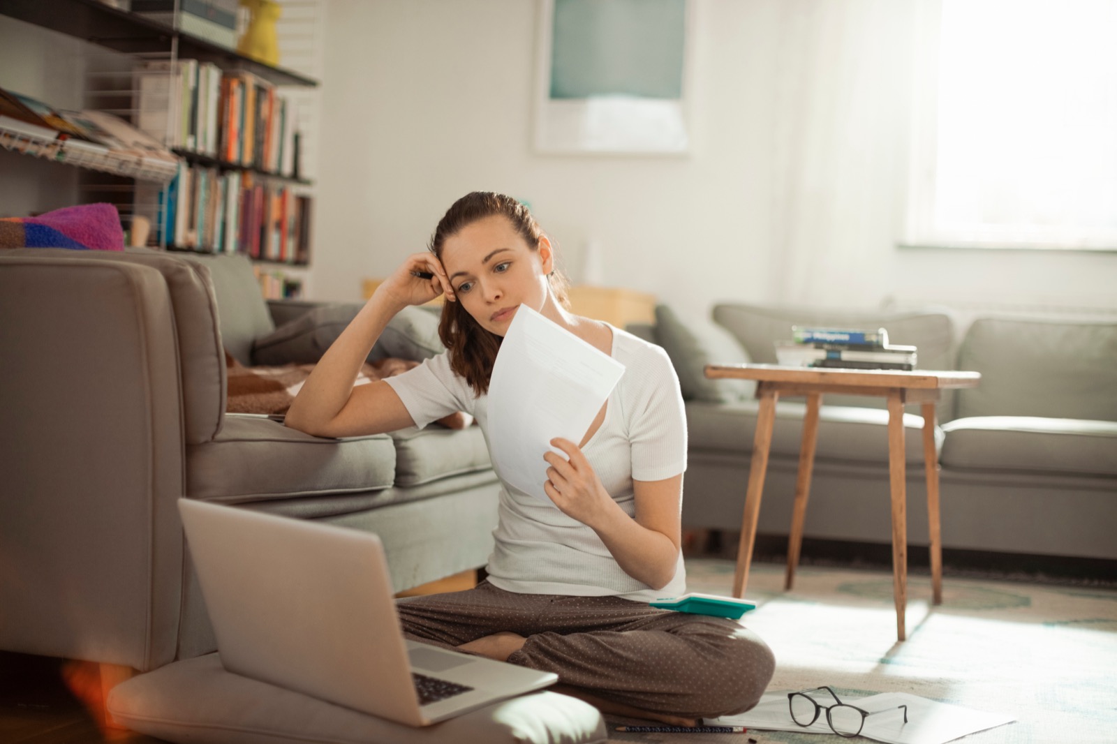 Woman on floor frustrated with finances displayed on laptop